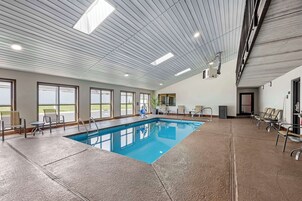 An indoor swimming pool with a view of the outdoors, ceiling lights, and seating areas.