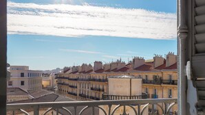 Un balcón con vista a una hilera de edificios bajo un cielo despejado y el sol brillando.