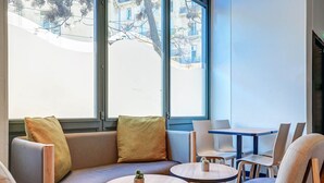 Un interior moderno con asientos, mesas y ventanas amplias que ofrecen vistas a edificios y árboles.