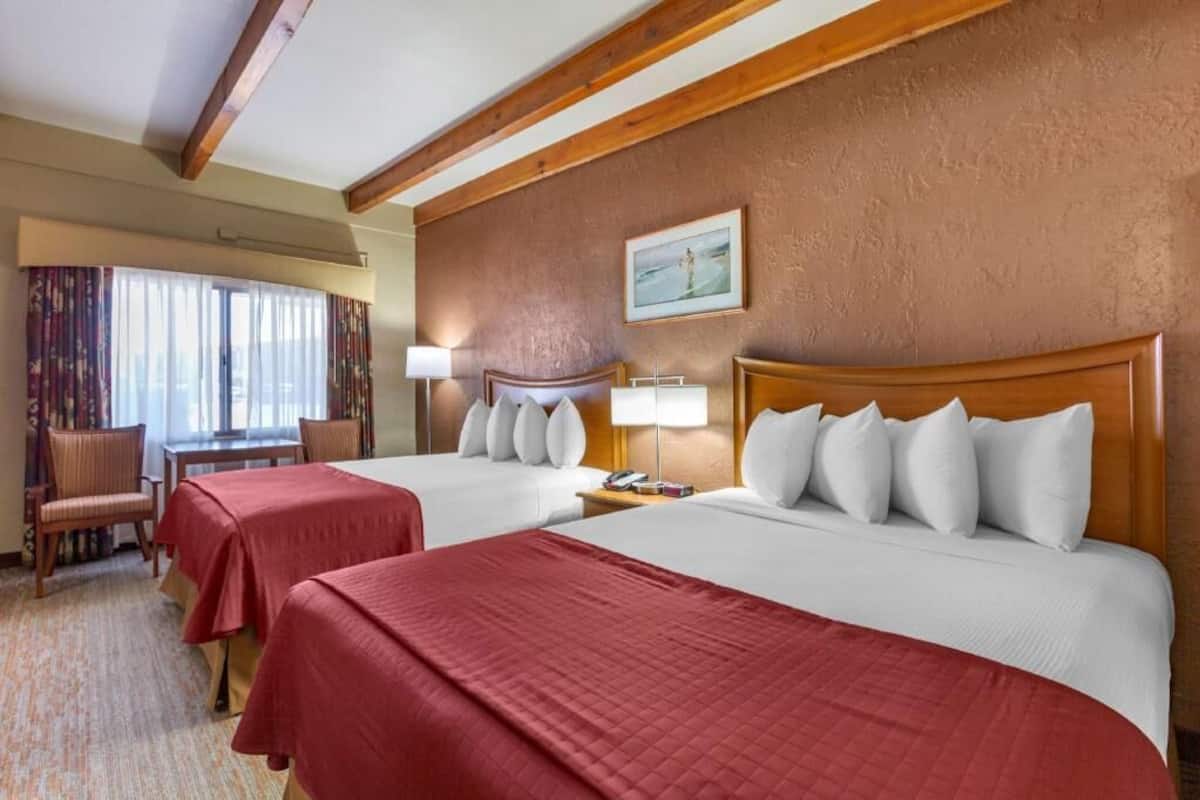 A hotel room with two beds, a desk, a chair, and a window with curtains.