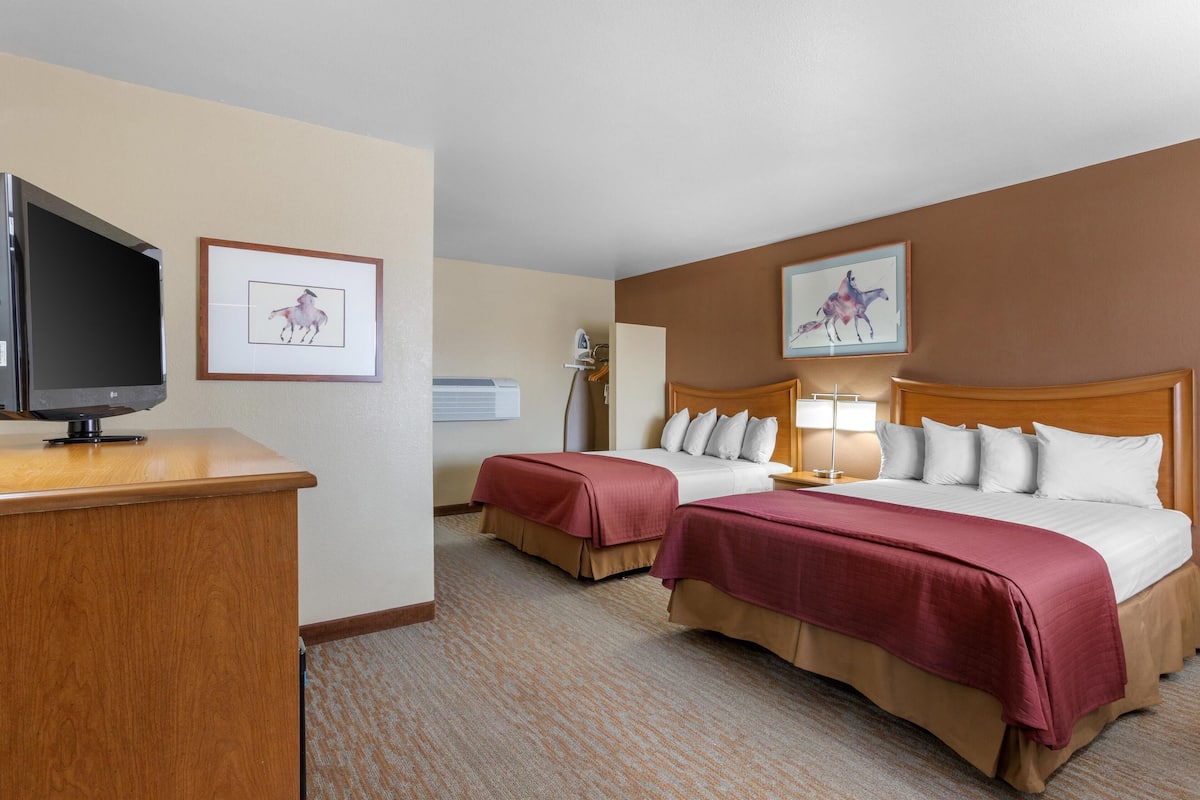 A hotel room with two beds, a desk with a television, and framed artwork on the walls.