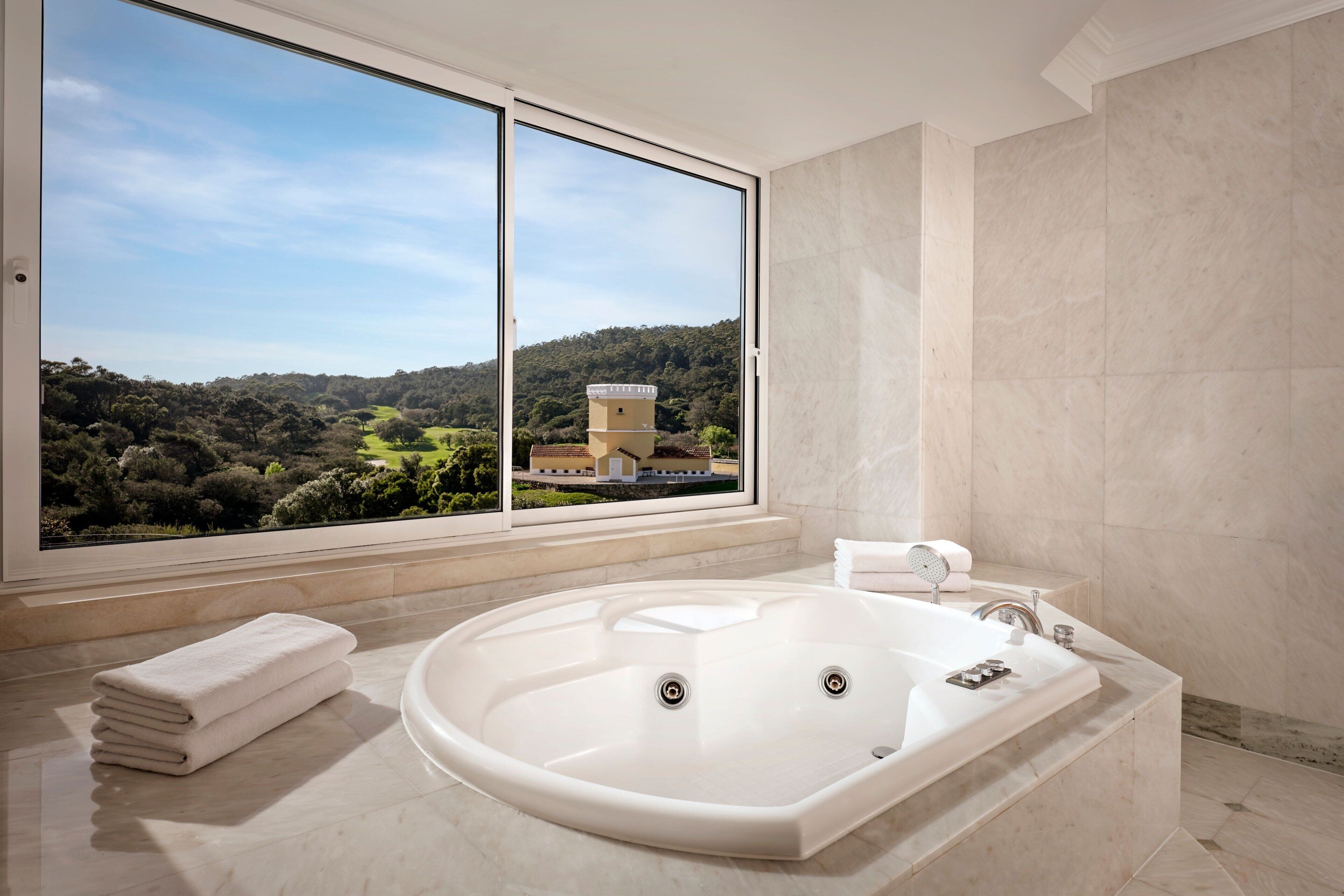 Uma casa de banho moderna com uma banheira grande, uma janela com vista panorâmica e uma toalha dobrada com cuidado.