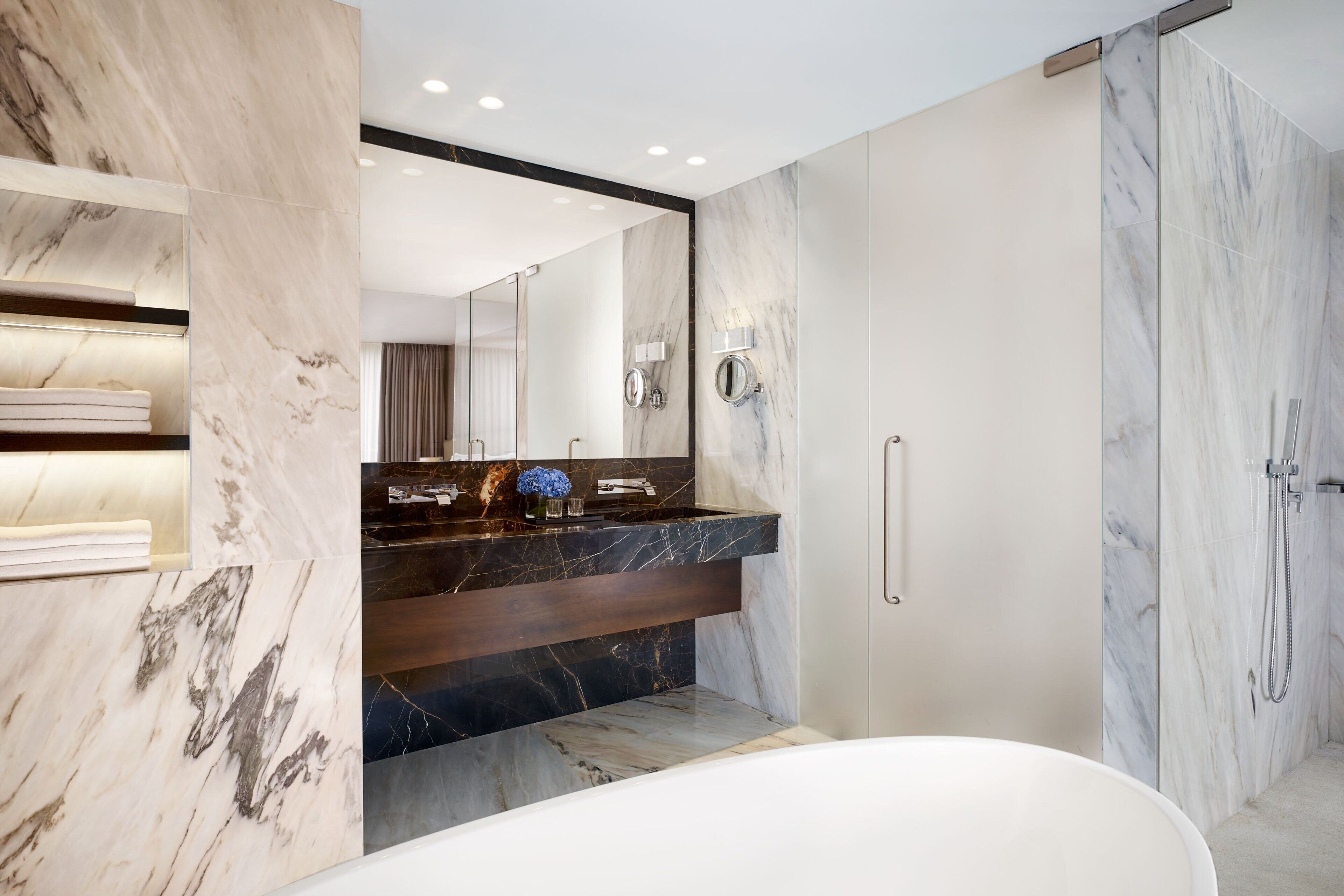 A modern bathroom with a marble vanity, a large mirror, and a walk-in shower.