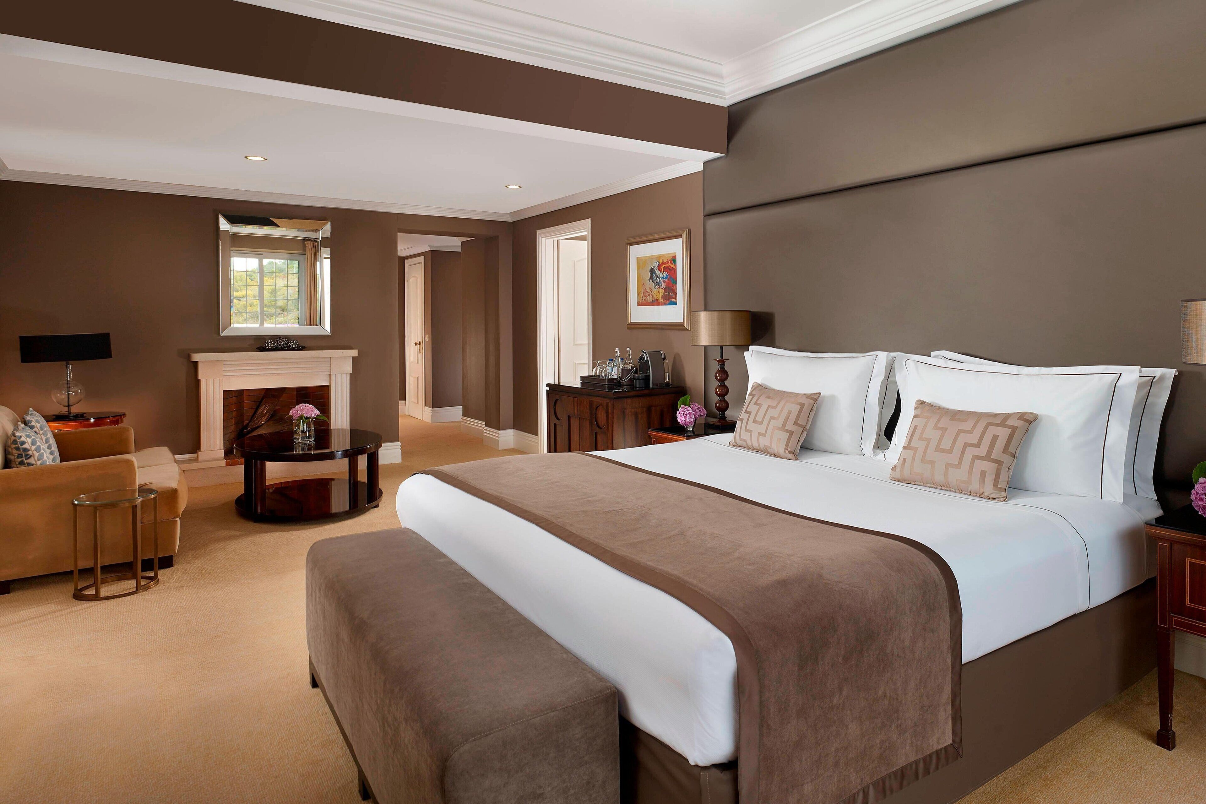 A spacious bedroom with a large bed, a fireplace, a sofa, and a dining table.