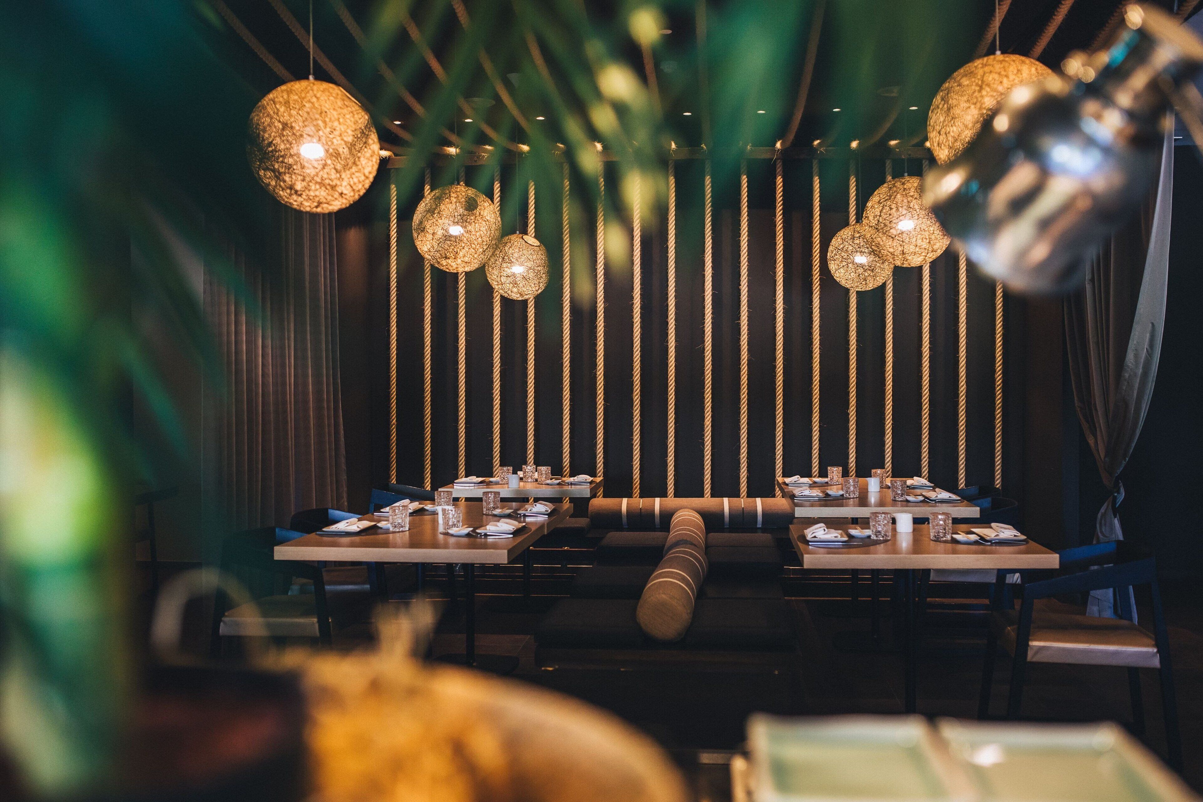 Un restaurante con una larga mesa dispuesta para comer, lámparas esféricas colgantes y decoraciones verticales similares a cuerdas.