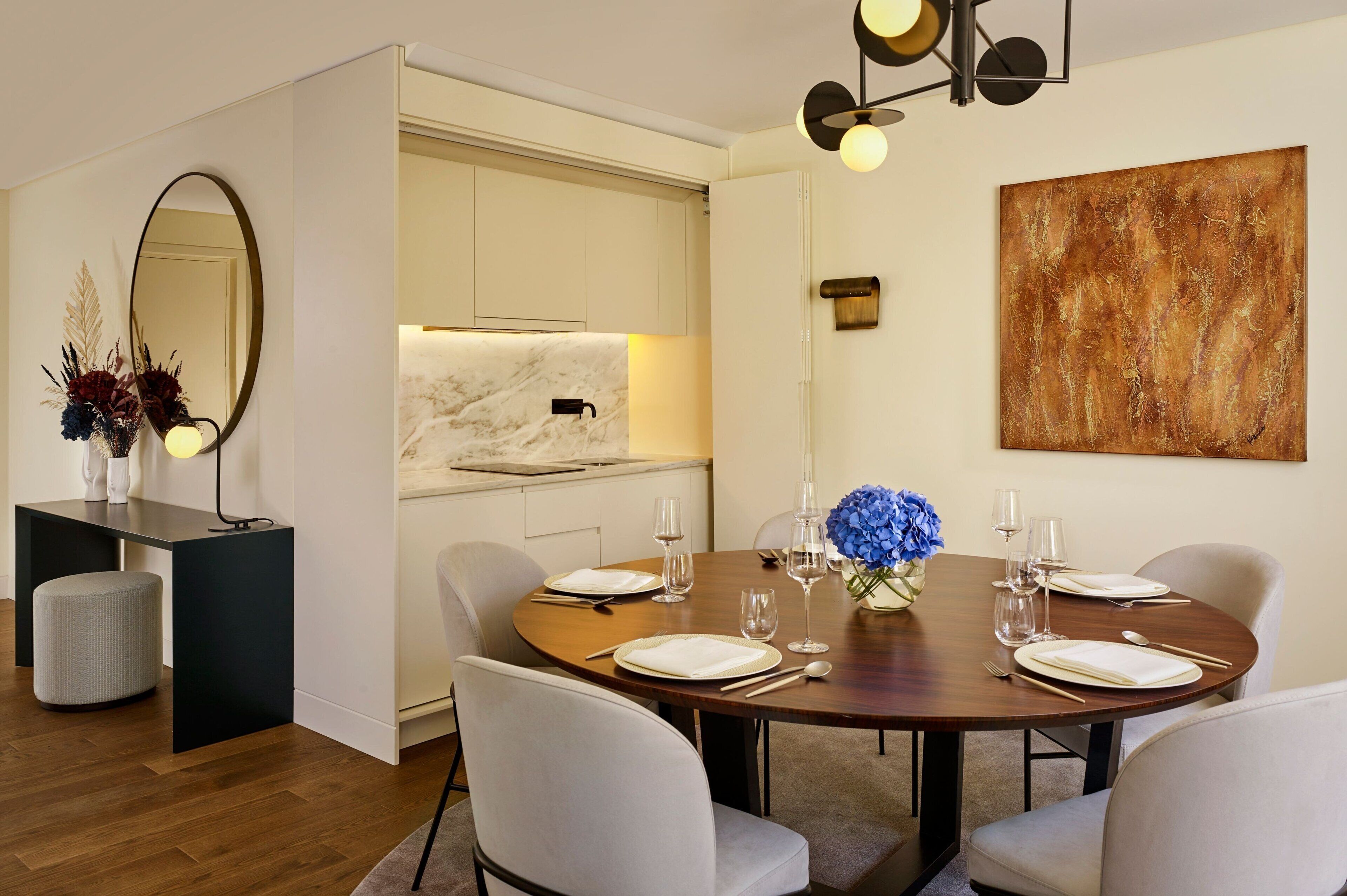 A dining area with a round table set for four, surrounded by chairs, a marble countertop, and a large abstract painting on the wall.