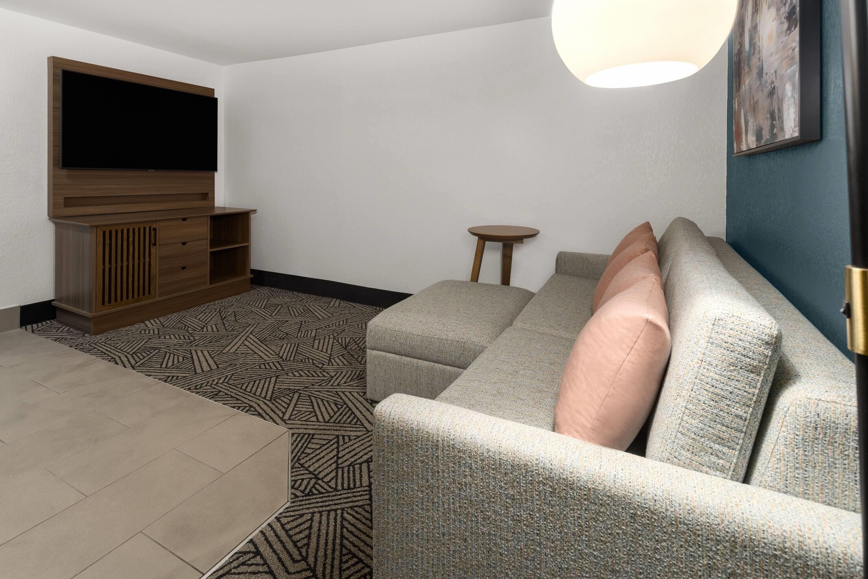 A living room with a sofa, a coffee table, a TV on a wooden stand, a small round table, and a patterned rug.