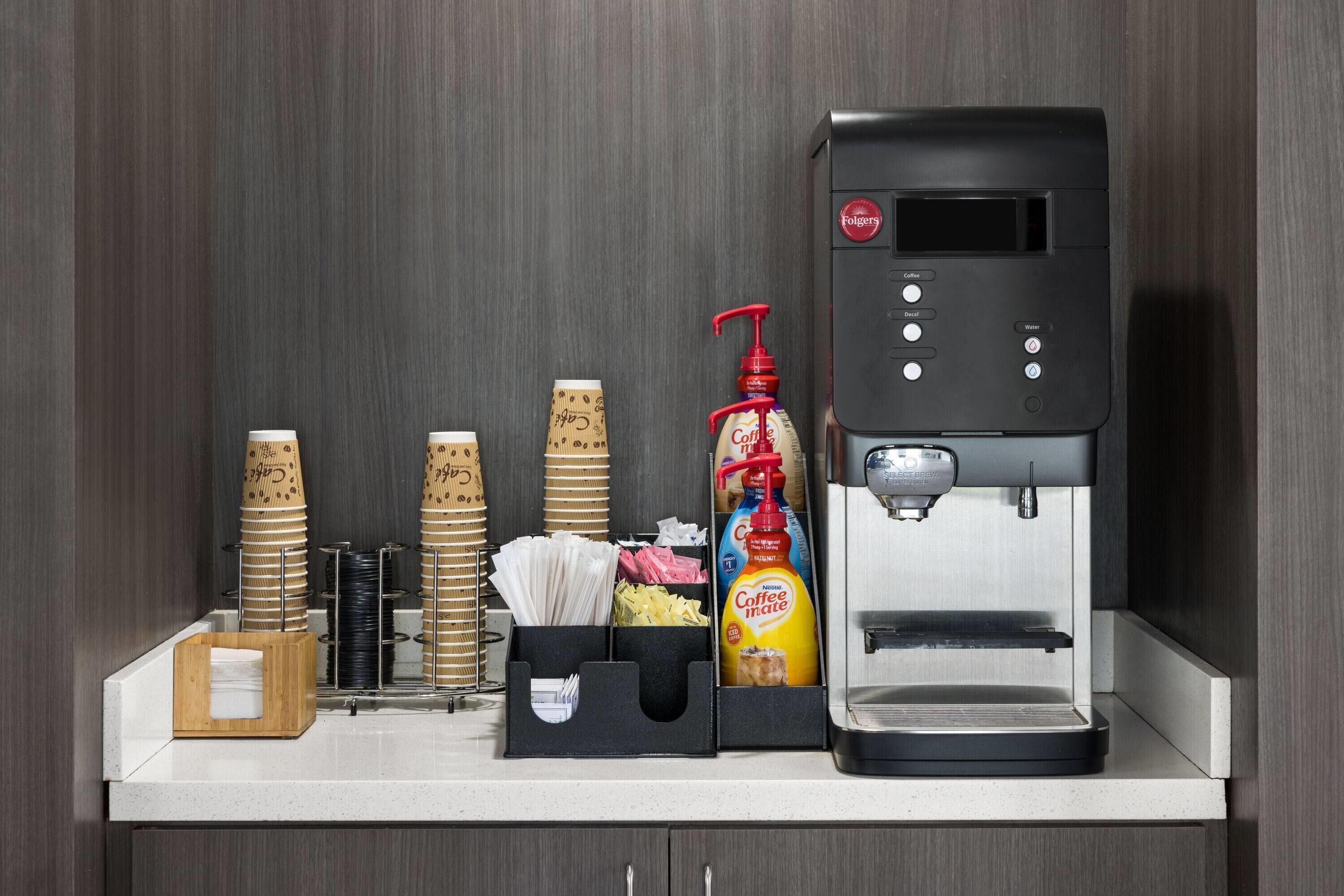 A coffee station with a Folgers coffee maker, disposable cups, and condiments.