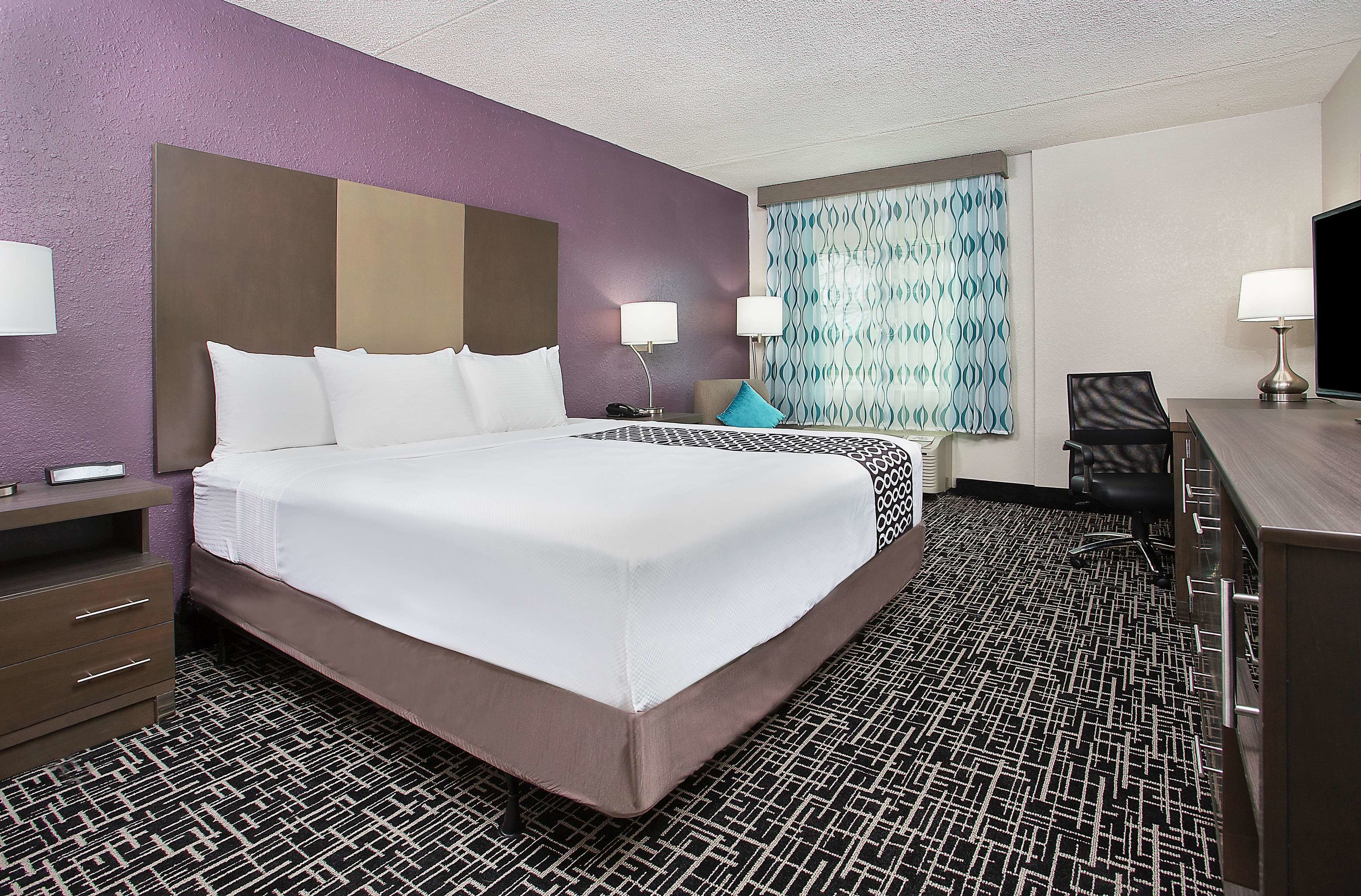 A hotel room with a large bed, a desk, two chairs, and a television.