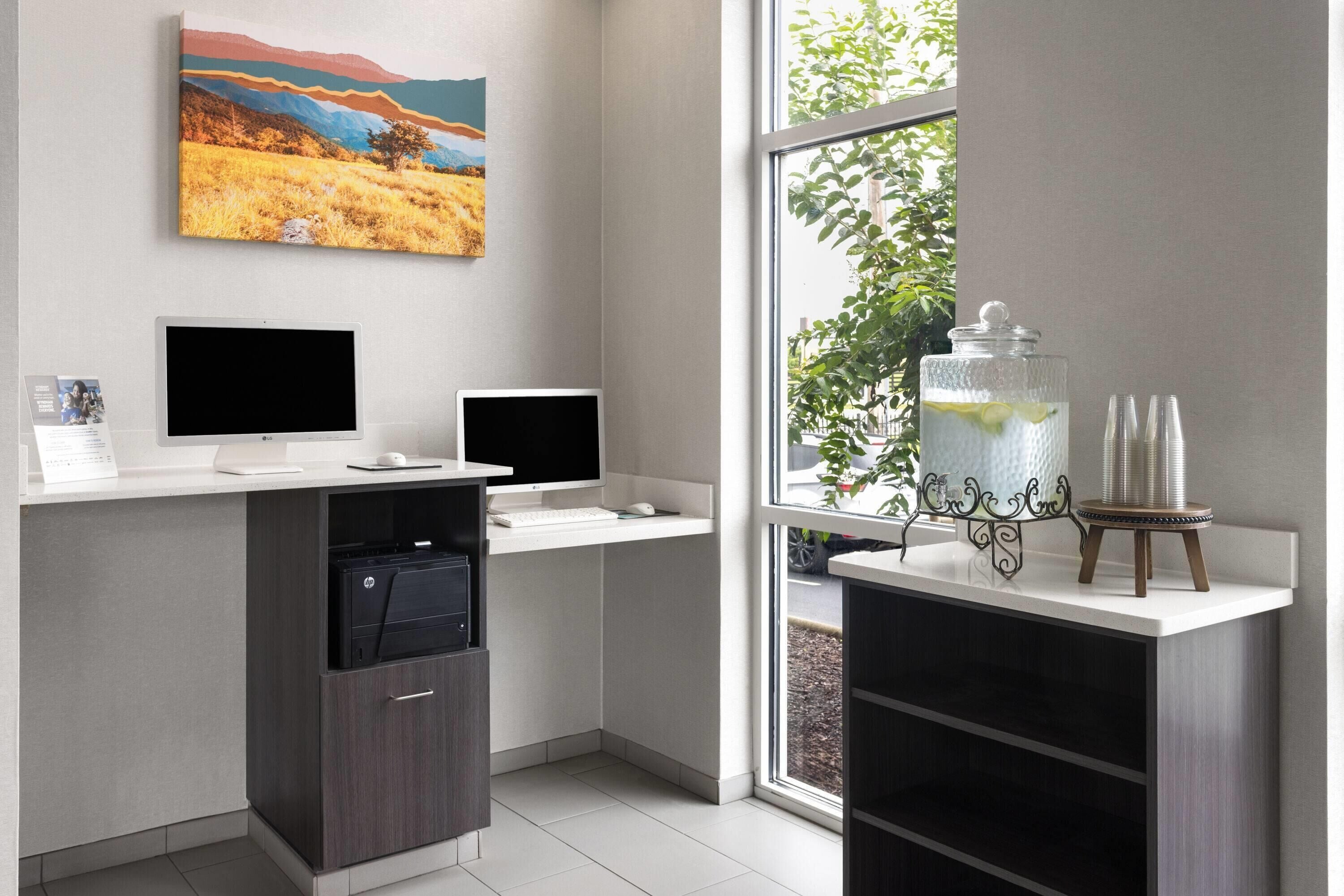 A modern kitchen with two monitors, a dishwasher, and a window with a view of greenery.