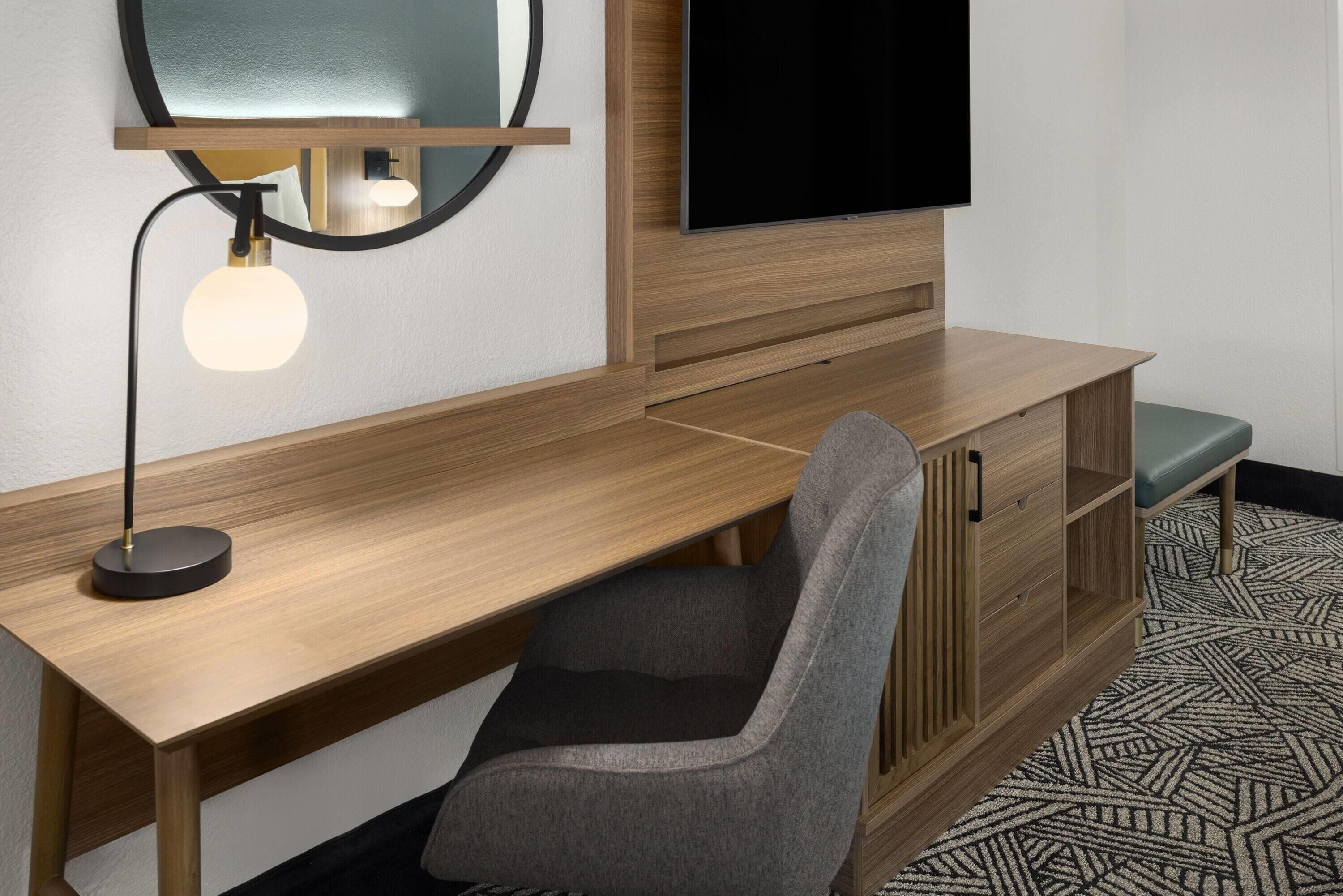 Un escritorio de madera con una silla, un televisor y un espejo.