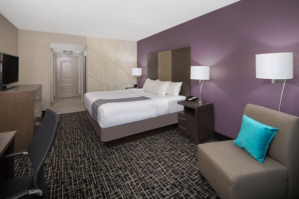 A hotel room with a bed, a desk, a chair, a TV, and a lamp.