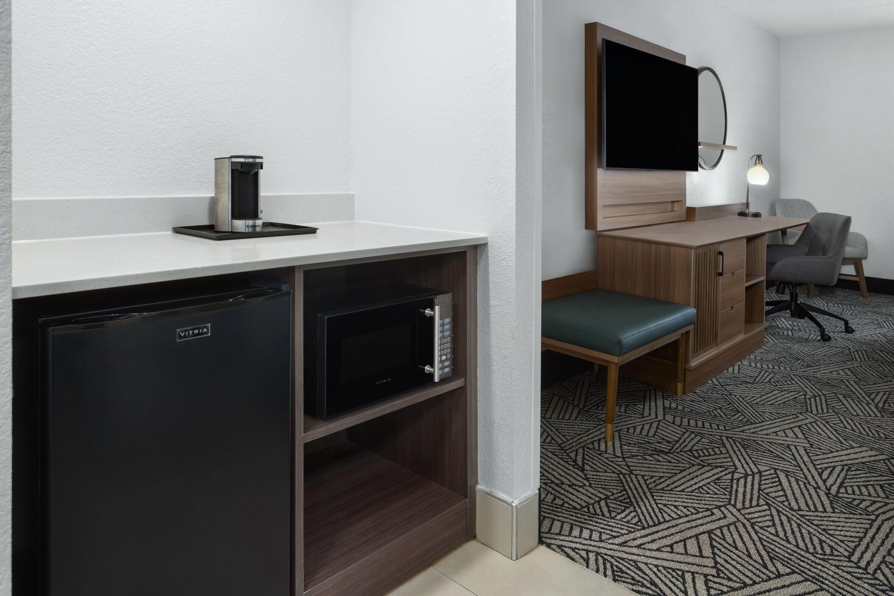 Une chambre d’hôtel compacte dotée d’une kitchenette, d’un téléviseur à écran plat, d’un bureau avec une chaise et d’un sol à motifs.