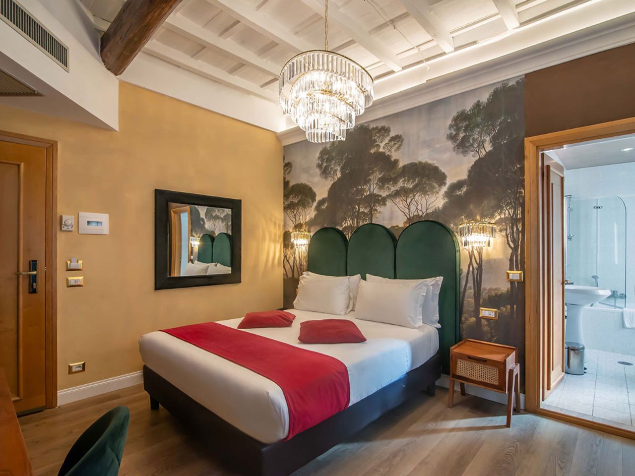 Een slaapkamer met een bed, een kroonluchter, een schilderij en een badkamer die door een geopende deur zichtbaar is.
