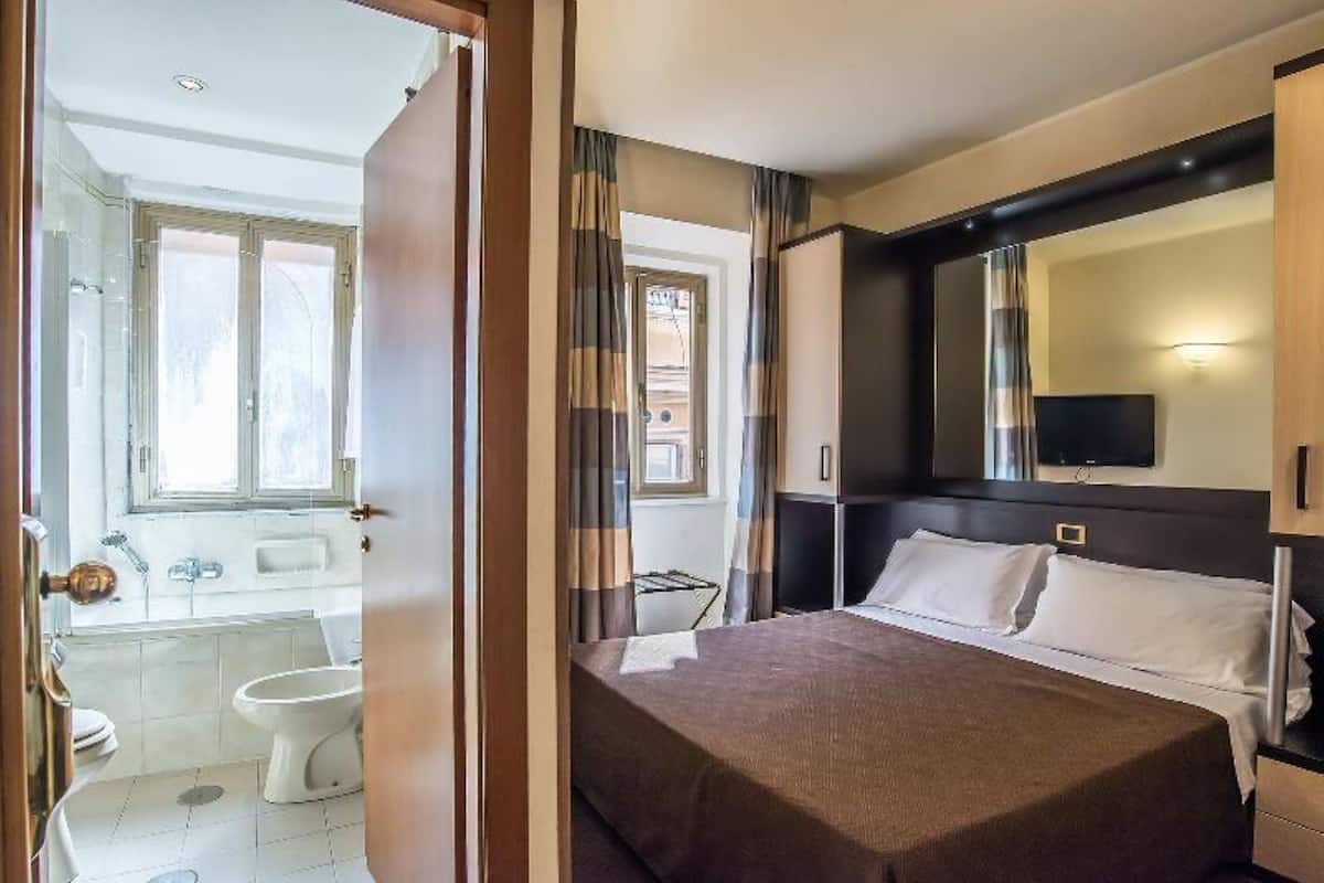 Une chambre d’hôtel équipée d’un lit, d’un grand miroir, d’une télévision et d’une salle de bain avec des toilettes et un lavabo.