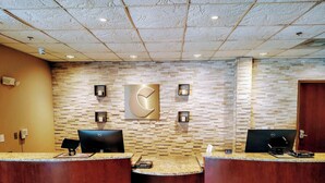 Un'area reception con due scrivanie, una parete decorata con un motivo in pietra e un soffitto con illuminazione a incasso.