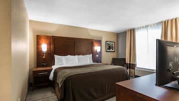 A hotel room with a large bed, a desk, a television, and a window with curtains.