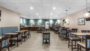 Un ristorante spazioso con diversi tavoli e sedie, una zona bancone e una parete blu decorata con quadri.