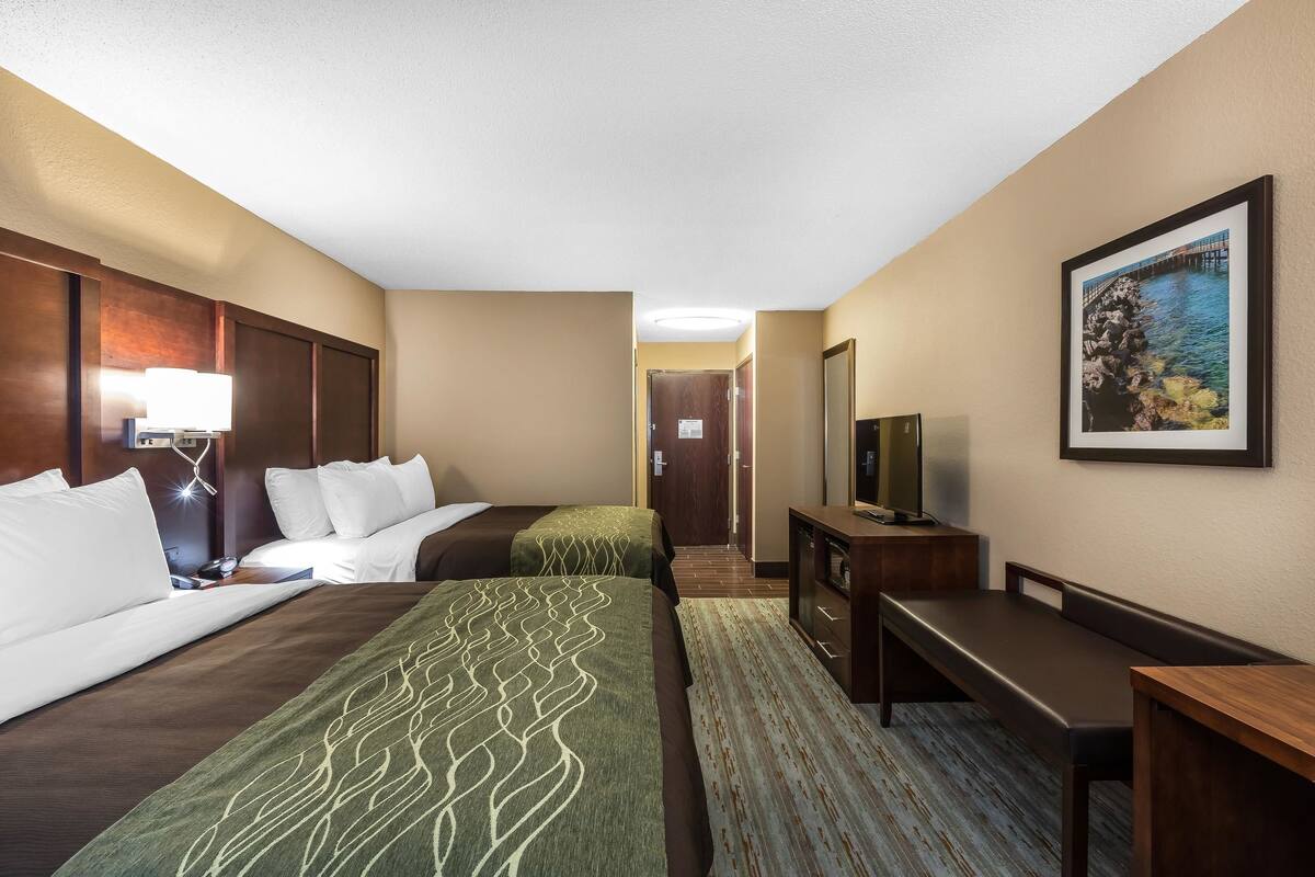 A hotel room with two beds, a desk, a television, and a framed picture on the wall.