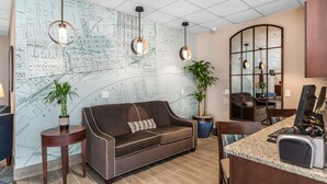 Un'accogliente hall d'hotel moderna con una grande mappa appesa al muro, un divano marrone, due tavolini con piante in vaso e una scrivania con un computer e un telefono.