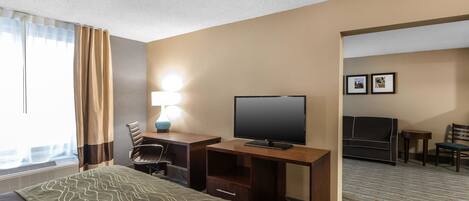 A hotel room with a bed, a desk with a TV, a chair, a lamp, and a sofa.