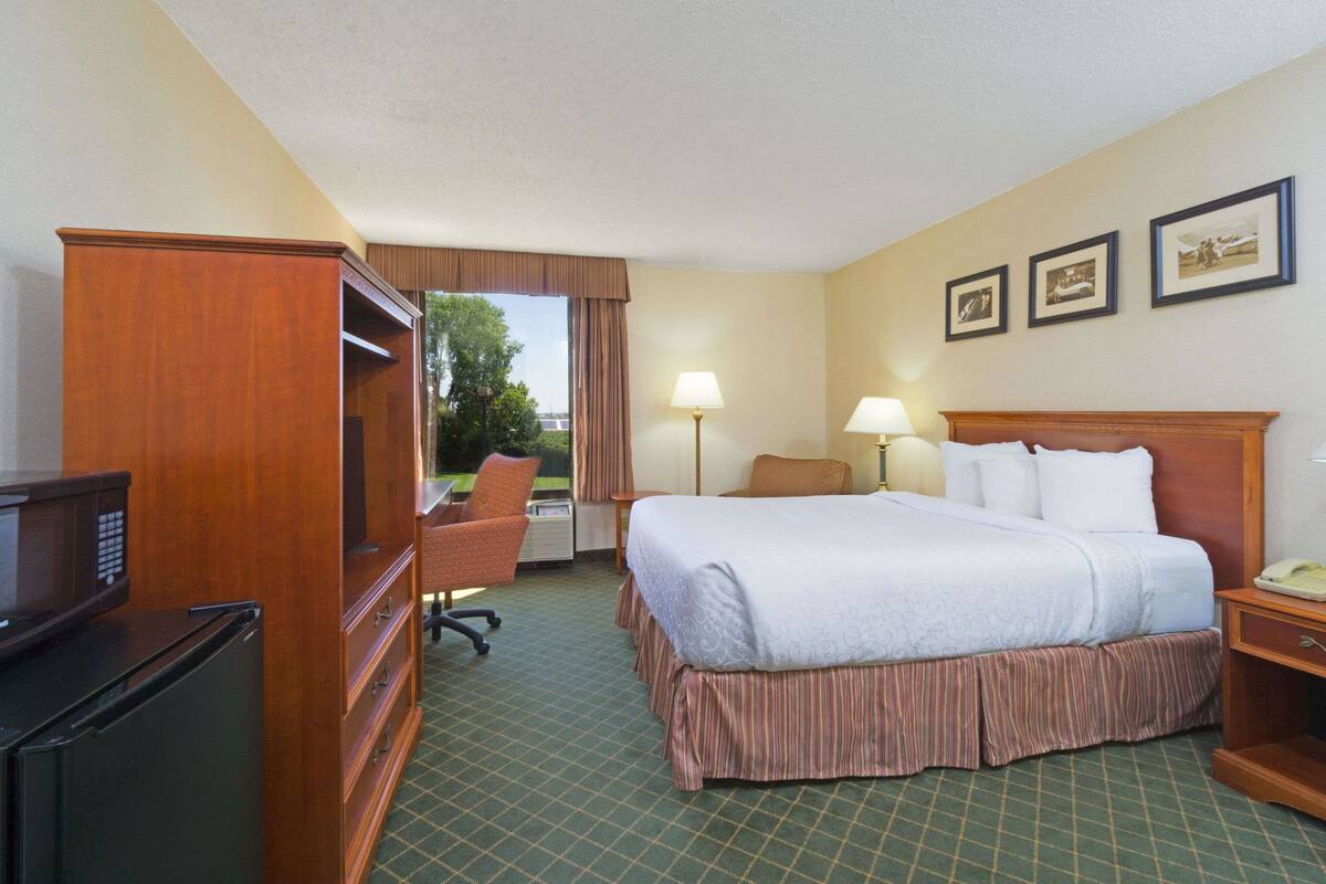 A hotel room with a bed, a desk, a chair, a television, and a refrigerator.