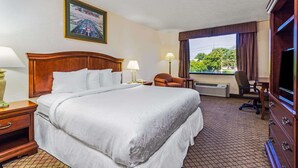 A hotel room with a large bed, a desk with a chair, a television, and a window with curtains. - Days Inn by Wyndham Columbus Airport (Columbus)