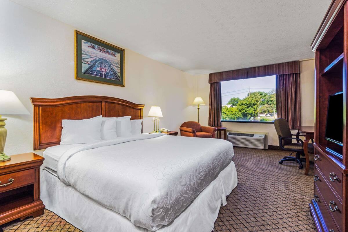 A hotel room with a large bed, a desk with a chair, a television, and a window with curtains.