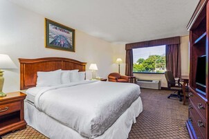 A hotel room with a large bed, a desk with a chair, a television, and a window with curtains.