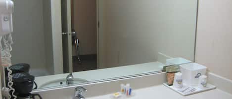 Un baño de hotel con un lavamanos blanco, una cafetera y artículos de aseo en la encimera.
