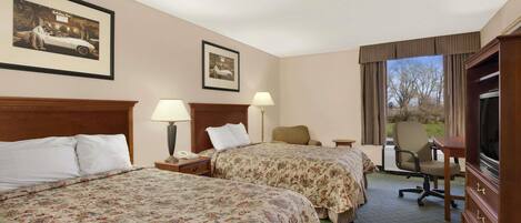 A hotel room with two beds, a desk, a chair, a television, and two framed pictures on the wall.