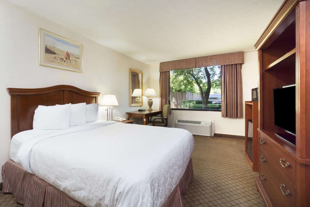 A hotel room with a large bed, a desk with a lamp, a television, and a window with curtains.