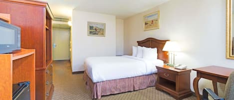 A hotel room with a bed, bedside table, lamp, chair, wooden wardrobe, and a television.