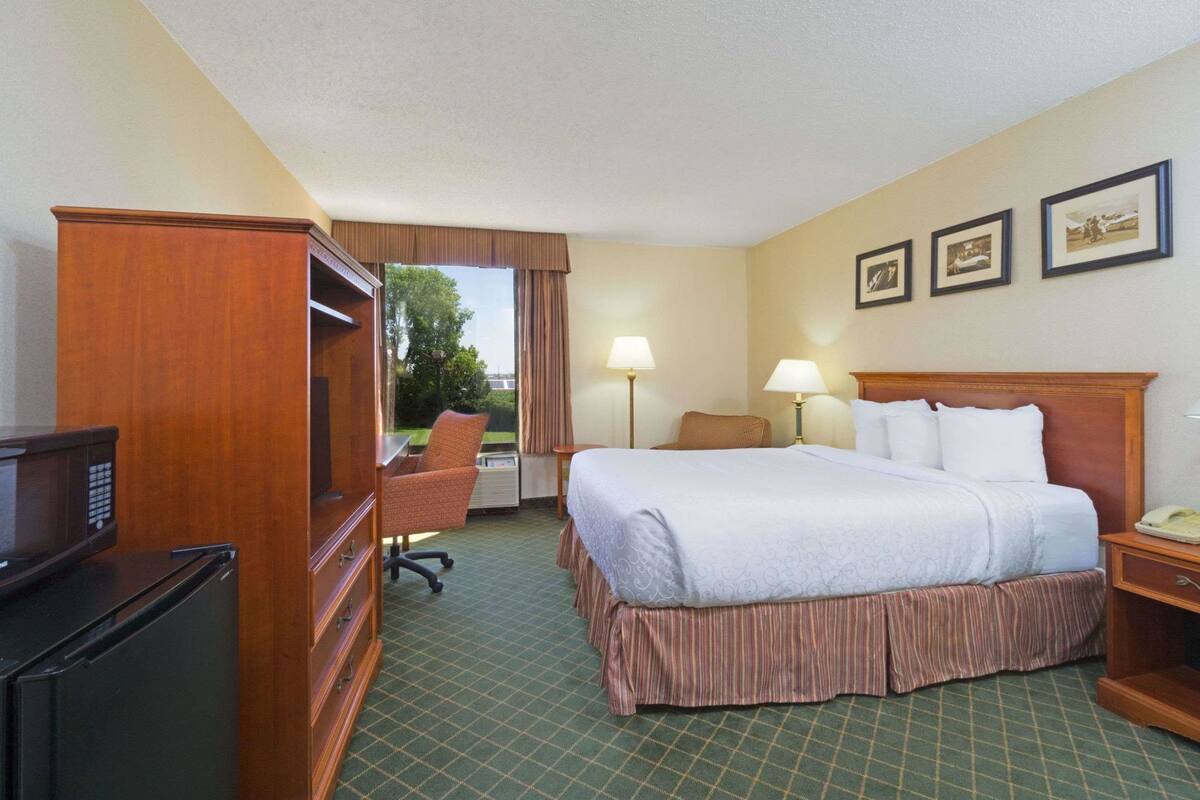 A hotel room with a bed, a desk with a chair, a television, a lamp, and a window with curtains.