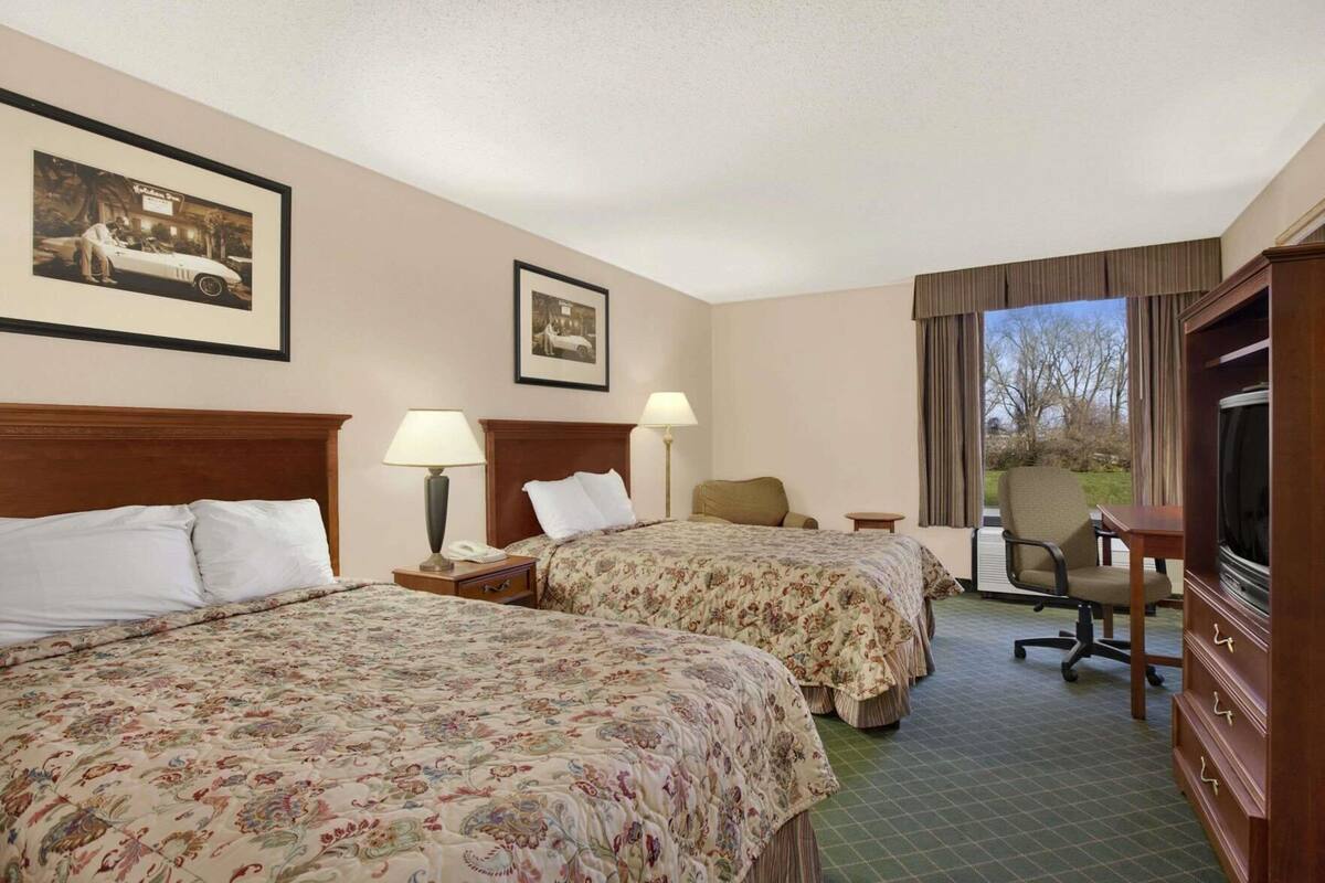 A hotel room with two beds, a desk, a chair, a television, and two framed pictures on the wall.