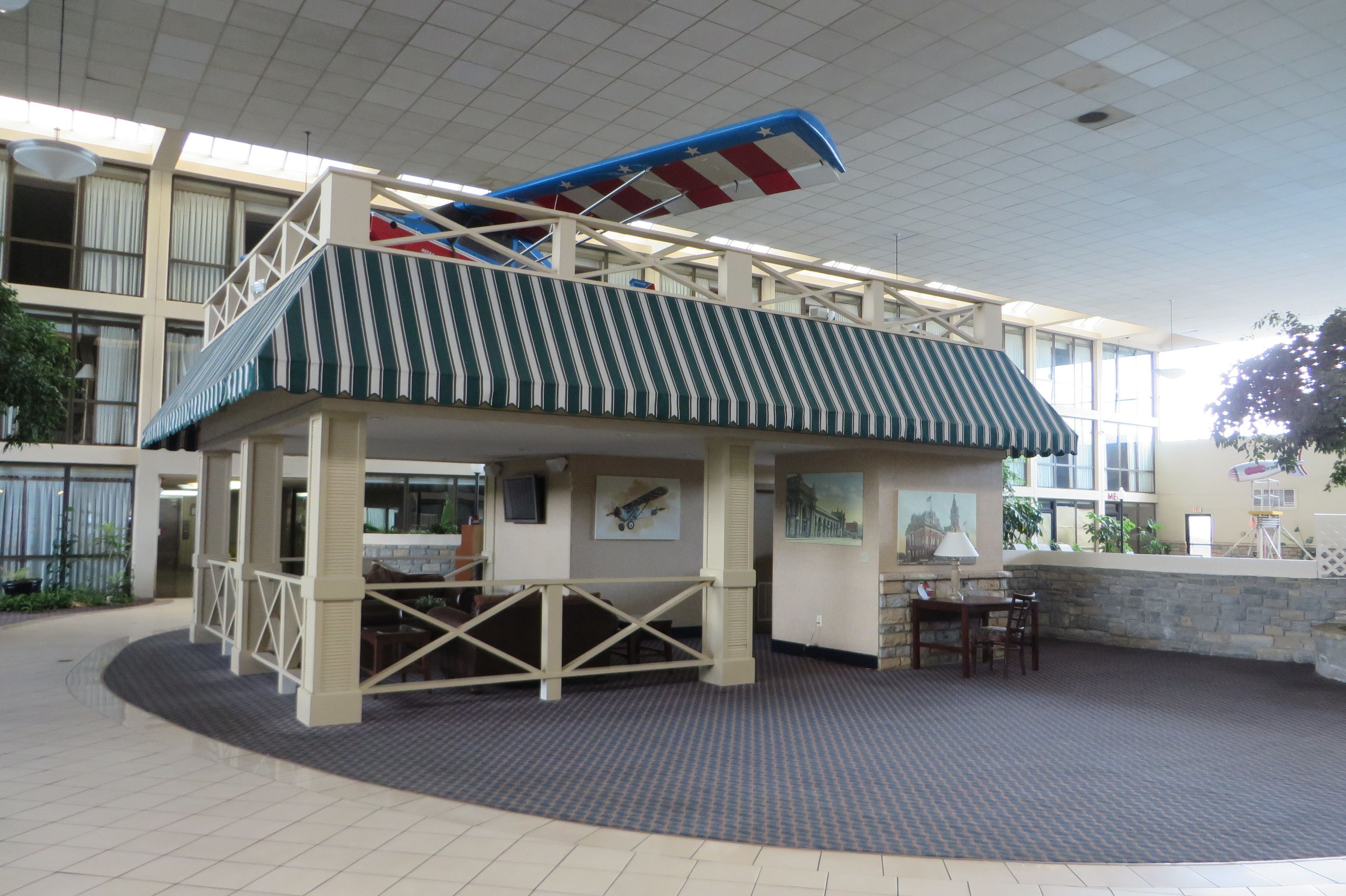 A covered outdoor area with a striped awning, a seating area with tables and chairs, and a staircase leading to an upper level.