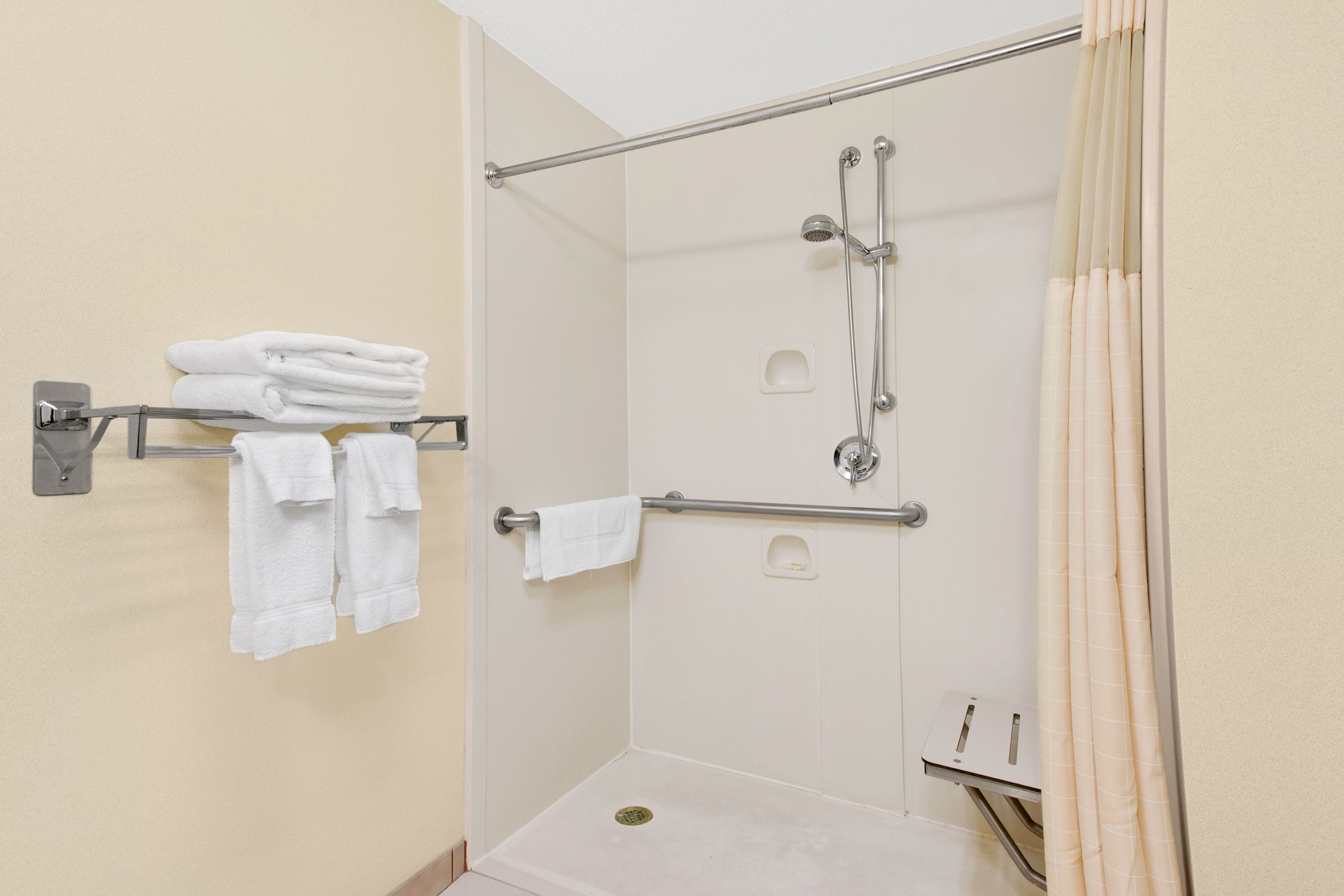 A shower with a glass door, a towel rack with folded towels, and a shower control panel.