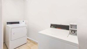 A laundry room with a front-loading washer and dryer, a control panel, and a small window above the dryer. - Days Inn by Wyndham Arlington Pentagon (Arlington)