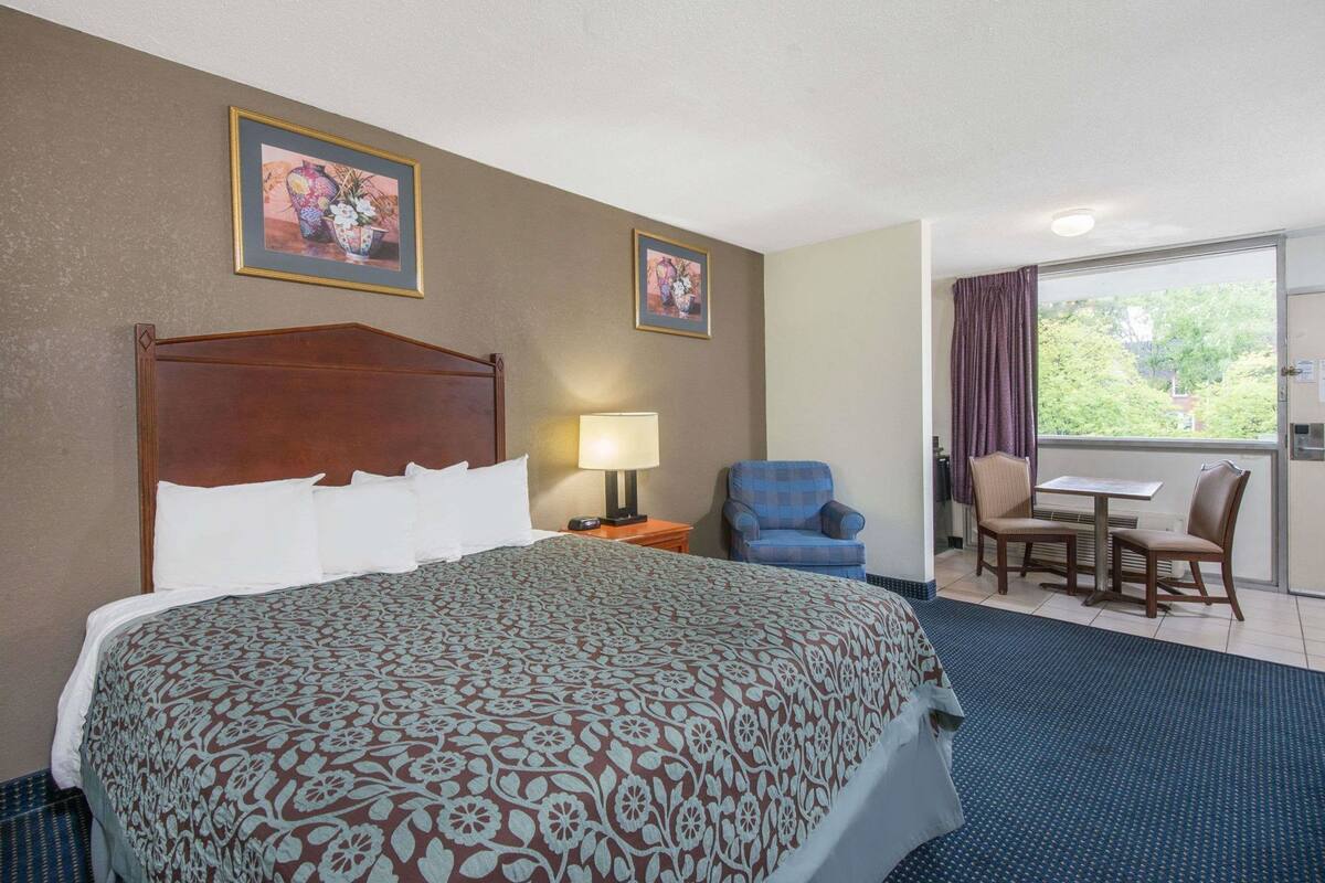 A hotel room with a large bed, a chair, a table, and two framed pictures on the wall.