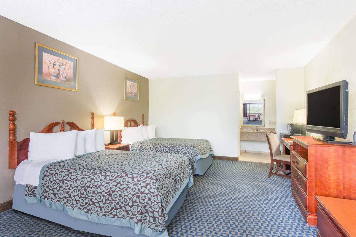 A hotel room with two beds, a television, a desk with a chair, and a bathroom visible in the background.