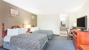 A hotel room with two beds, a television, a desk with a chair, and a bathroom visible in the background.