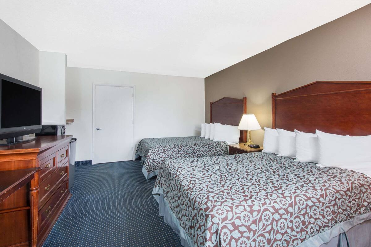 A hotel room with two beds, a TV, a dresser, and a lamp.