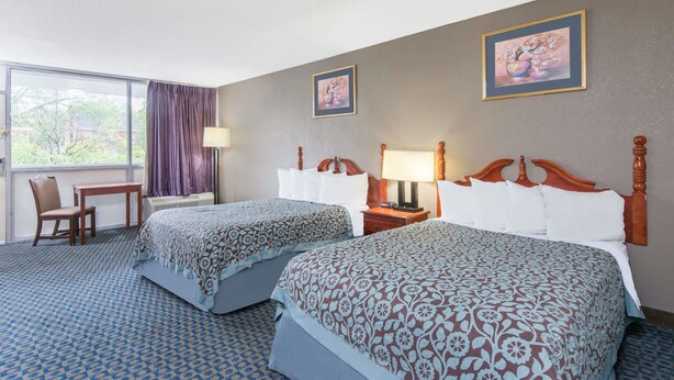 A hotel room with two beds, a desk, a chair, a window with curtains, and two wall-mounted lamps. - Days Inn by Wyndham Arlington Pentagon (Arlington)