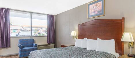 A hotel room with a large bed, a chair, a window with curtains, and a painting on the wall.
