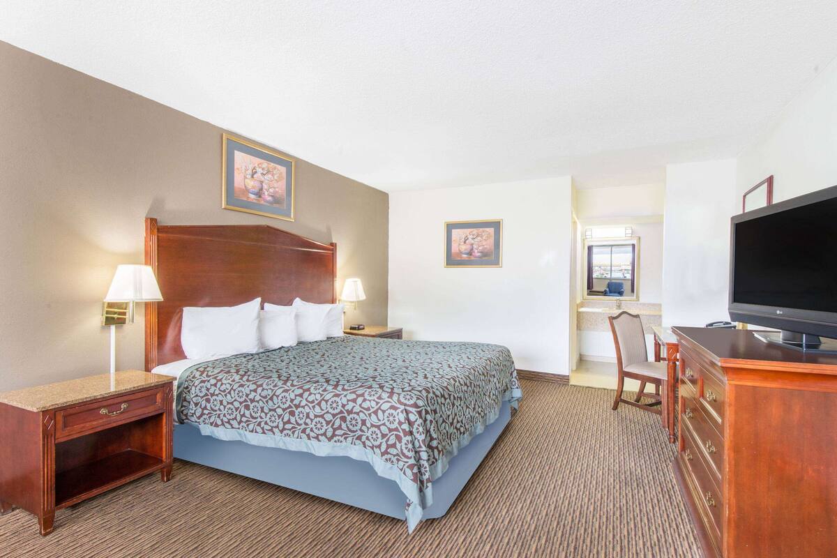 A hotel room with a bed, a desk, a television, and two framed pictures on the wall.
