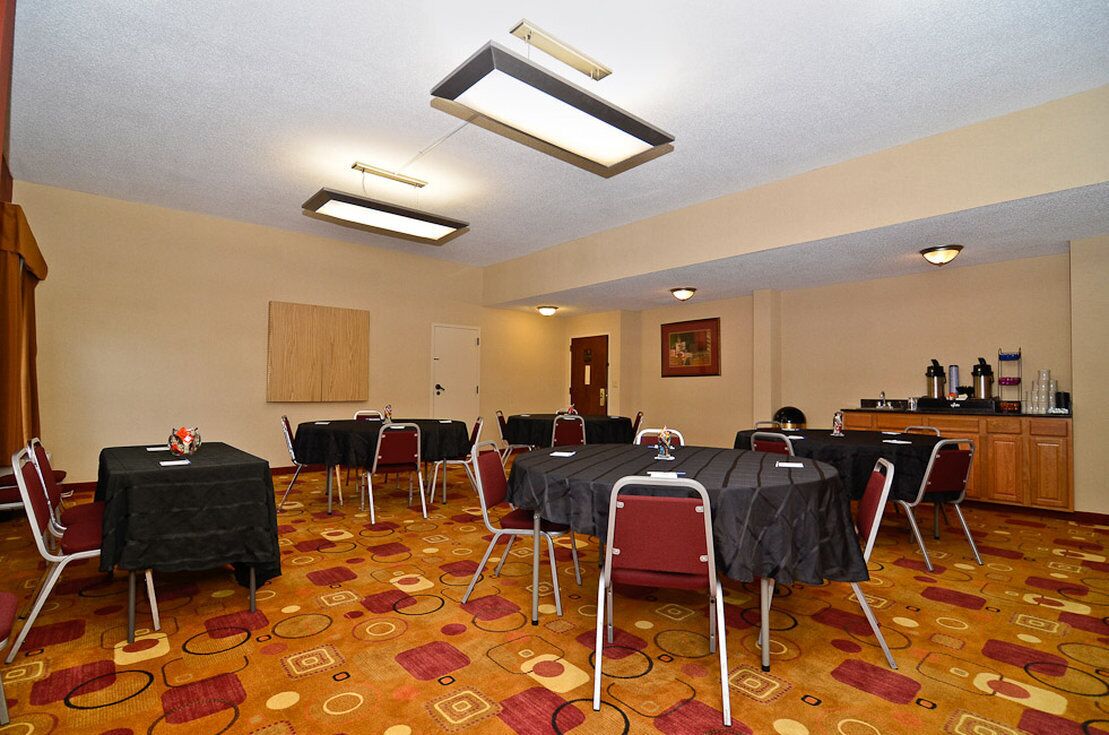 A conference room with tables and chairs, a wooden door, and a cabinet with items on it.