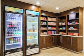 Automat område med to drikkemaskiner og hylder fyldt med snacks og drikkevarer.