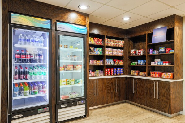 A vending area with two beverage dispensers and shelves stocked with snacks and beverages.