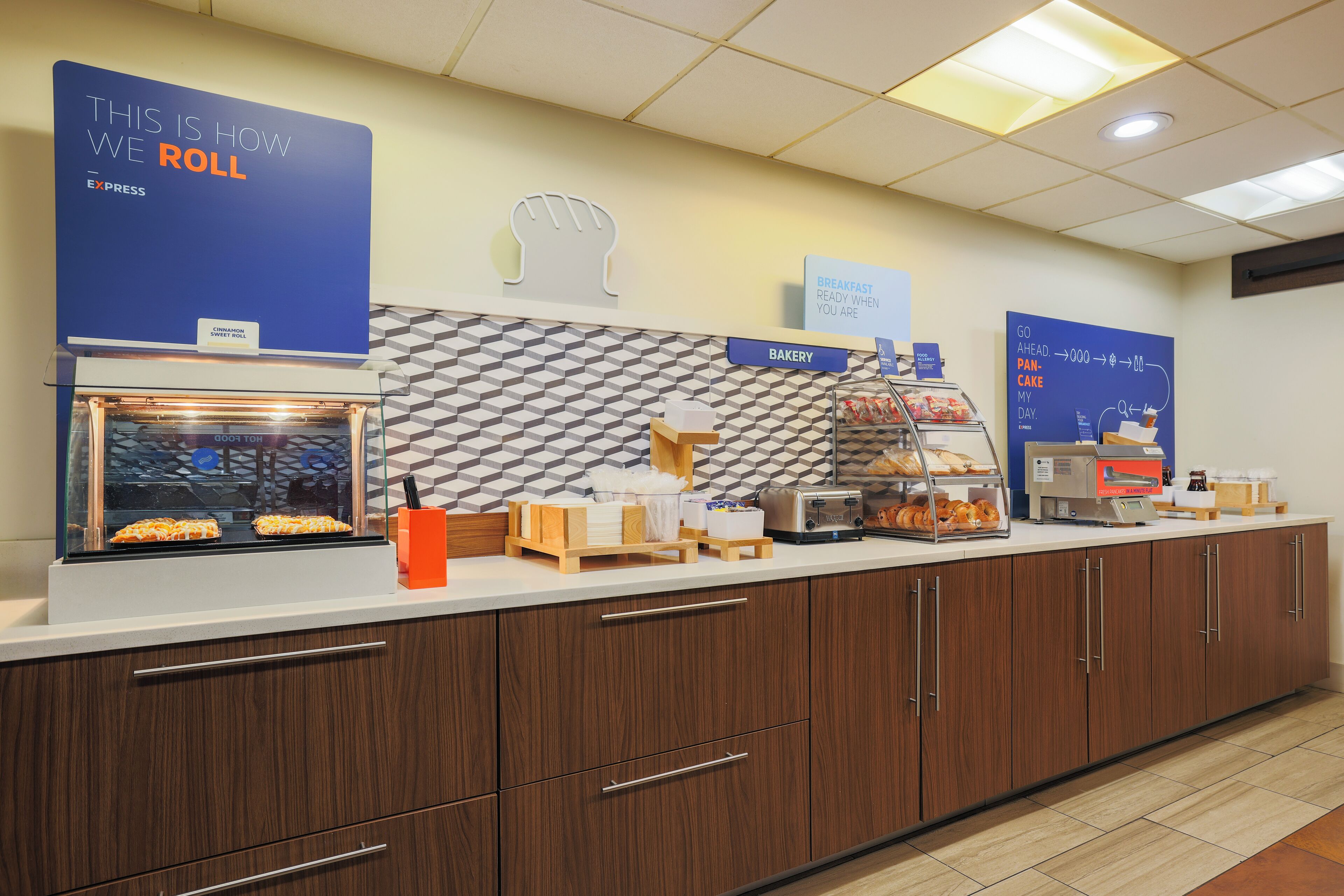 A breakfast bar with a sign indicating the roll-in service, a toaster, and a display of pastries.