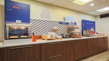A breakfast bar with a sign indicating the roll-in service, a toaster, and a display of pastries.